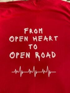 Back of red shirt John Cressler wore to walk Pittsburgh marathon, with text saying From Open Heart to Open road with an illustration of an EKG line below.